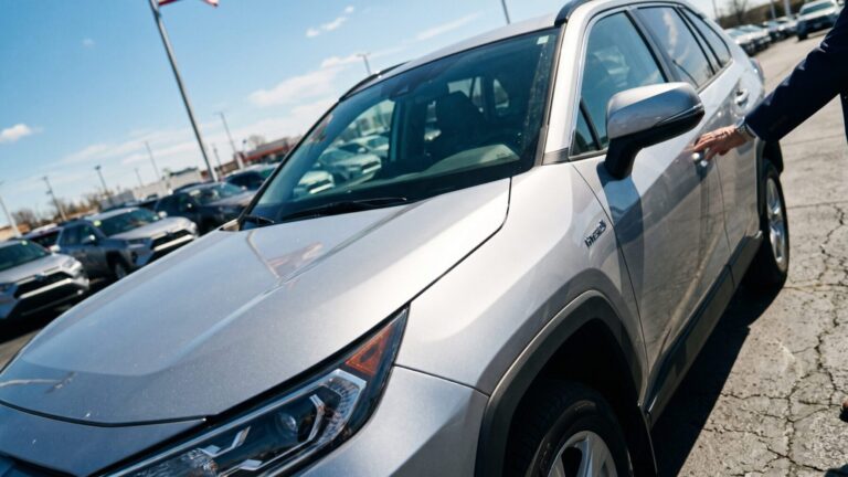 A hybrid SUV on a dealership lot under hard midday sun, hybrid vehicles