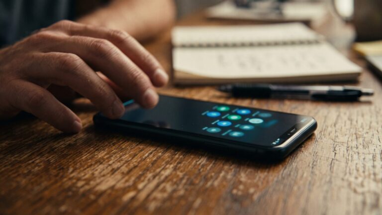 Smartphone notifications glowing on a desk, hand reaching toward the screen, phones buzzing