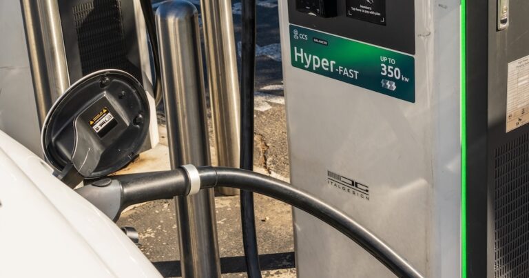 Hand plugging a NACS connector into an electric car at a charging station, charging network