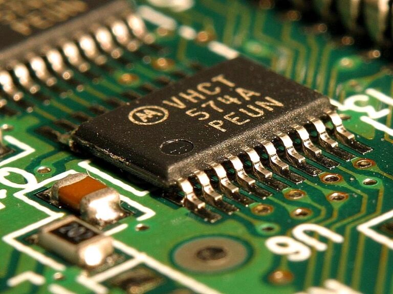 Automotive chips on a circuit board with a car assembly line in background, europe s