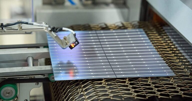 Worker inspects a silicon wafer inside a solar factory clean room, wafers