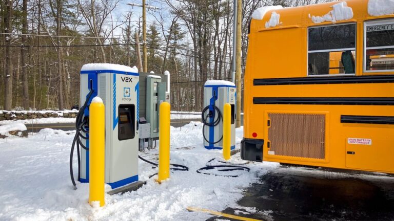 Electric school bus plugged into vehicle-to-grid charging cable at dusk, massachusetts school