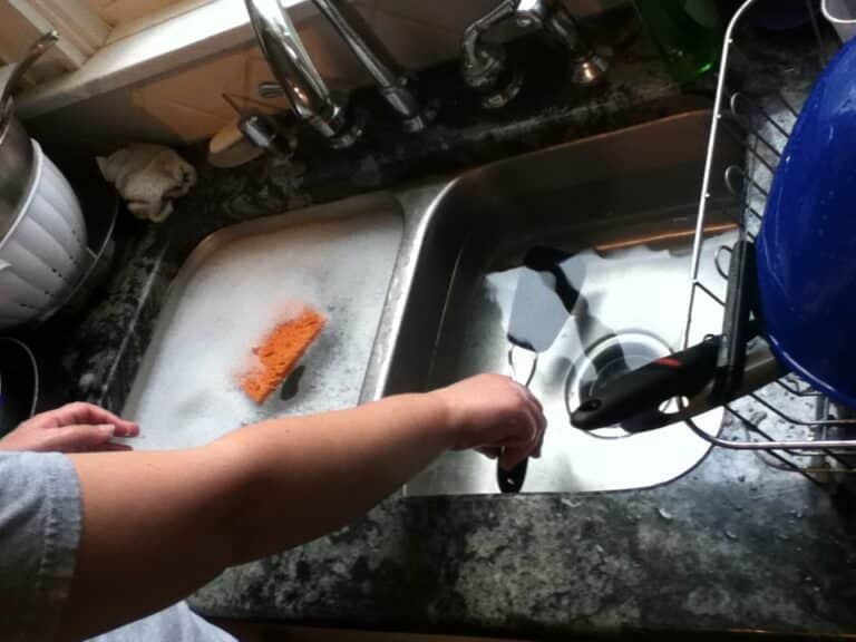 Hands washing dishes during a mindful dishwashing study, sink full